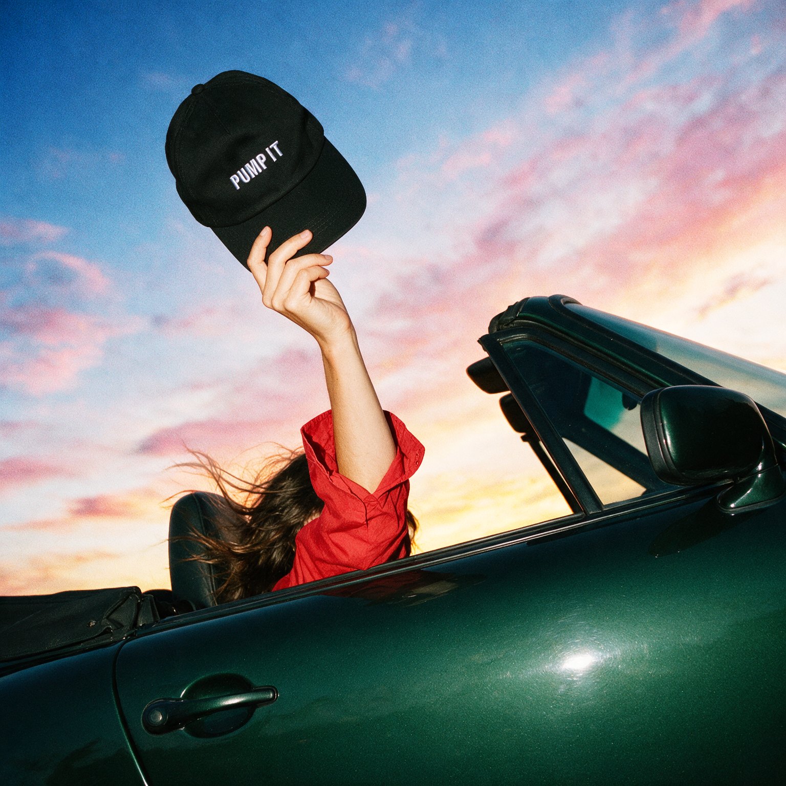 Figure holding a cap above a green car