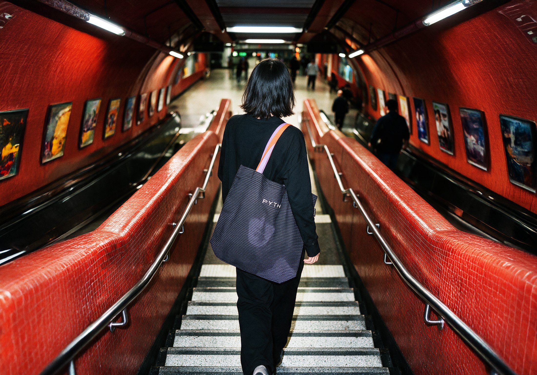 Figure carrying a tote bag on an escalator