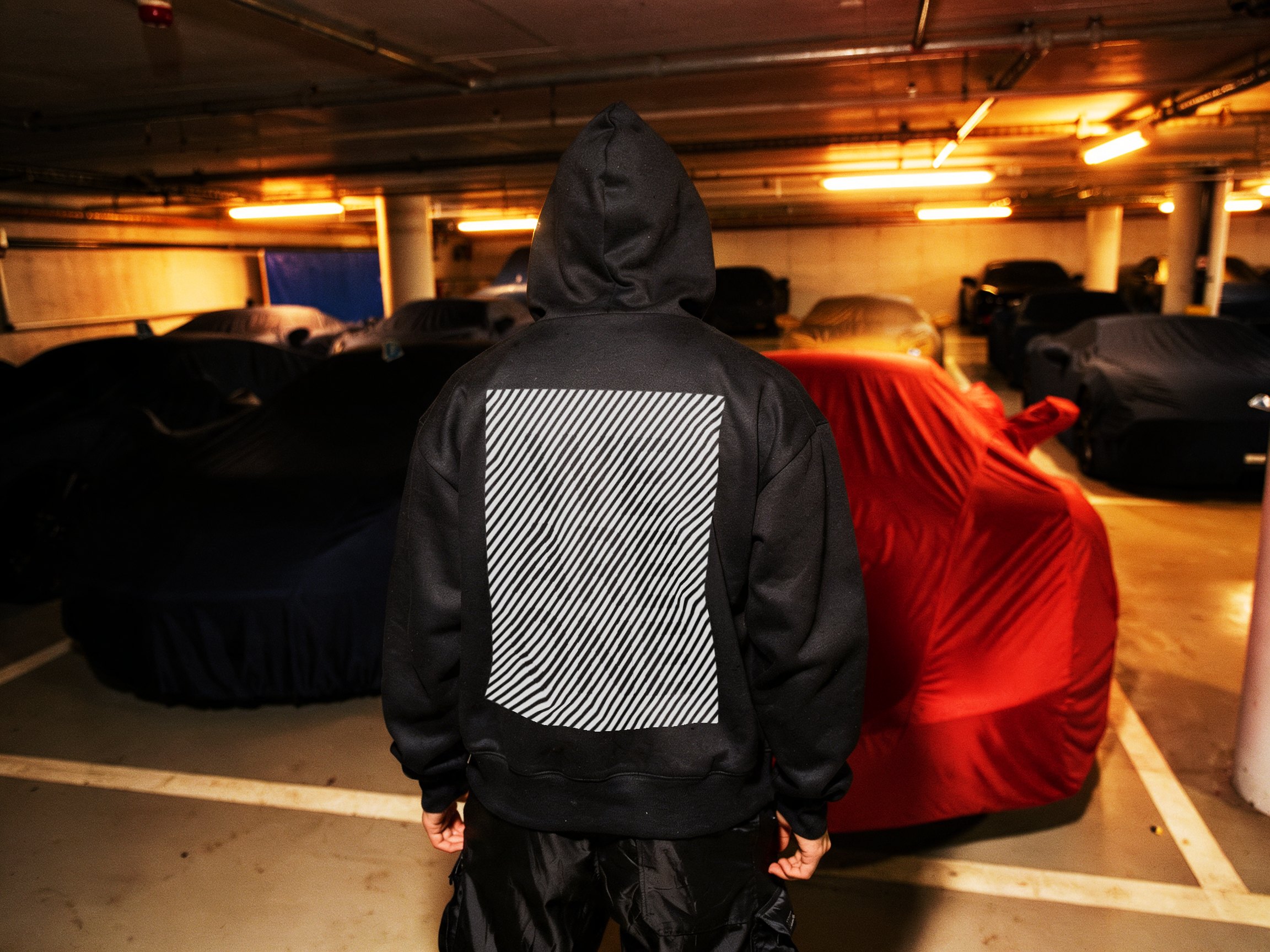 Figure wearing a dark hoodie beside a red car