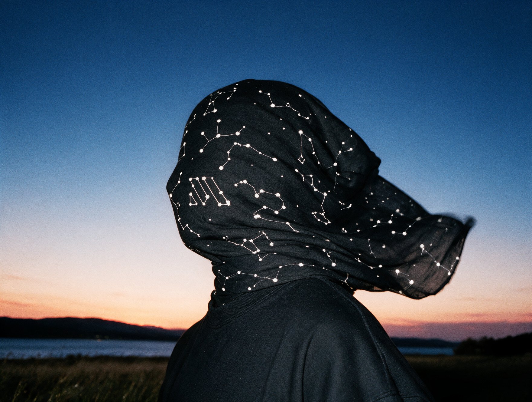 Figure wearing a patterned scarf against a twilight sky