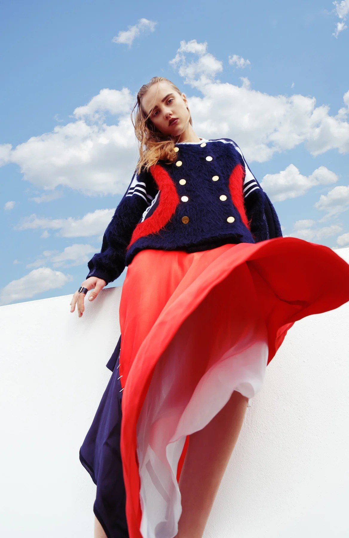 Figure in a red skirt viewed from below against clouds