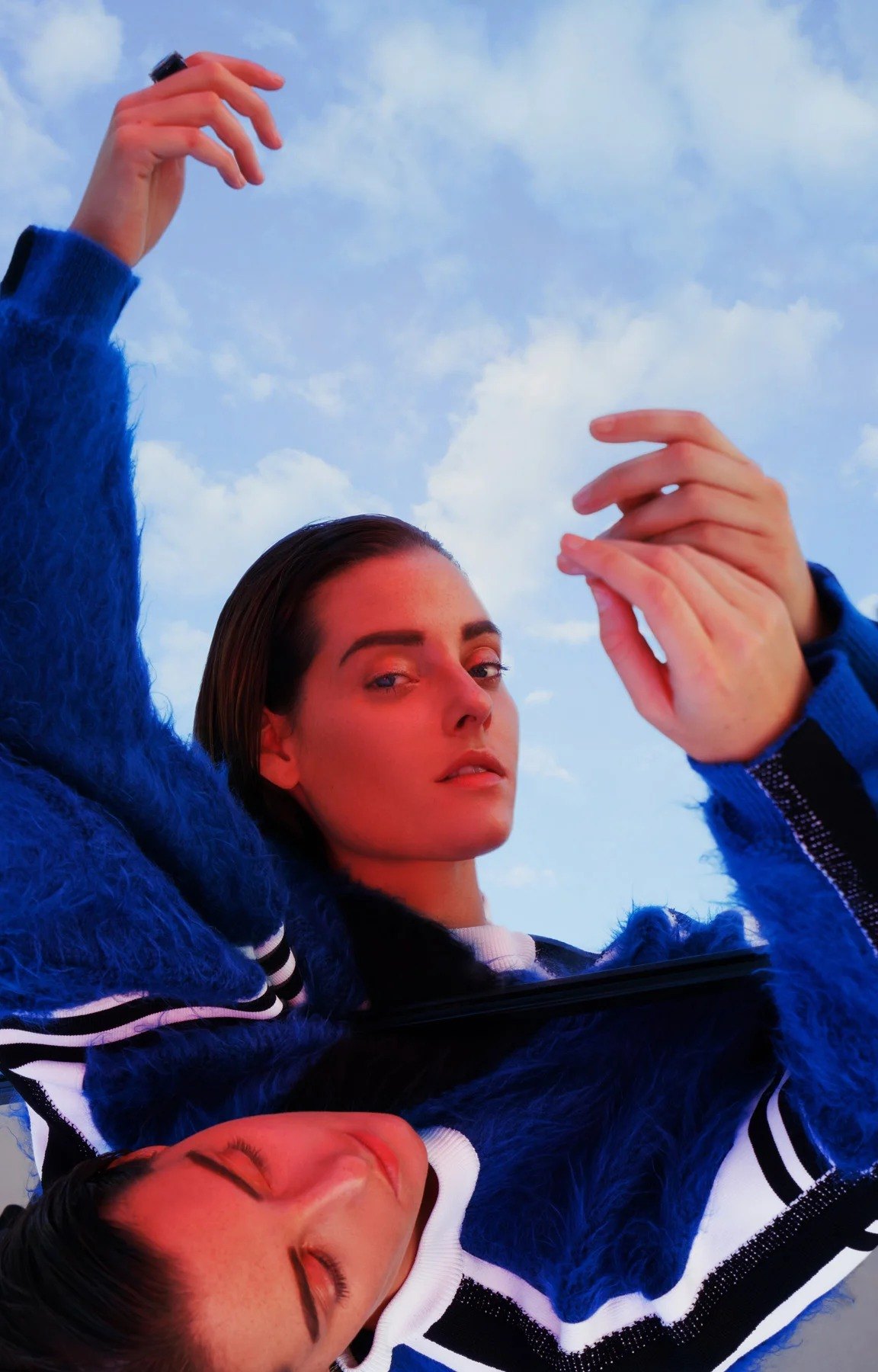 Close-up of a face and raised hands against the sky