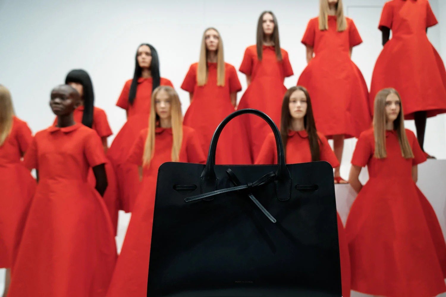 Figures in red arranged behind a large black handbag