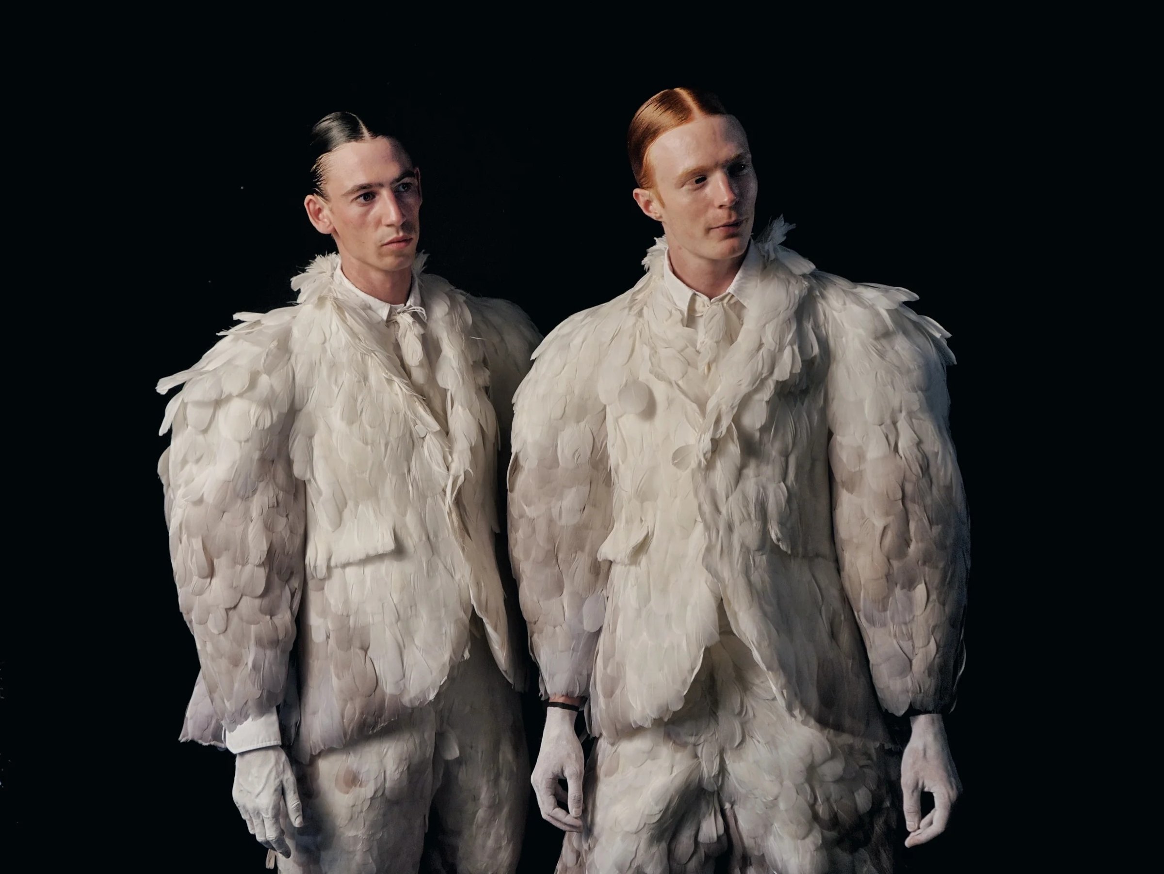Two figures in textured pale outfits against black