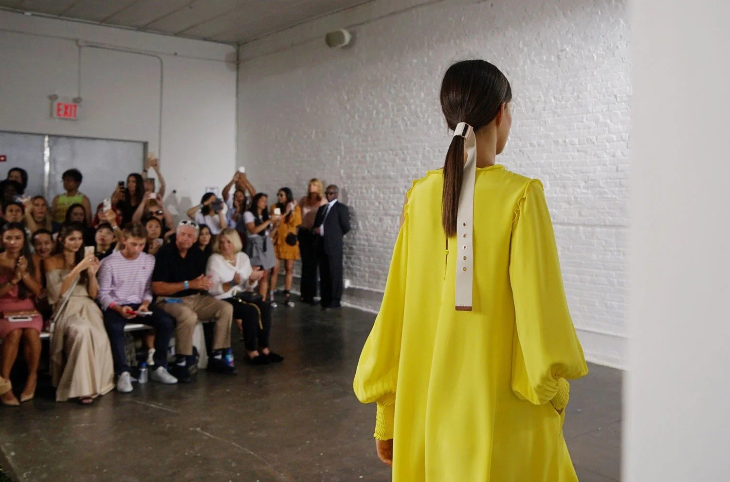 Figure in a yellow dress walking past a seated audience