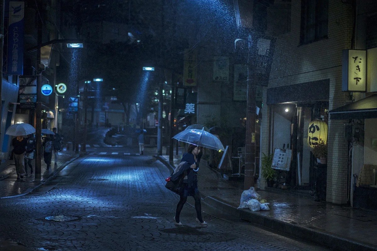 Figure with an umbrella crossing a blue-lit street at night