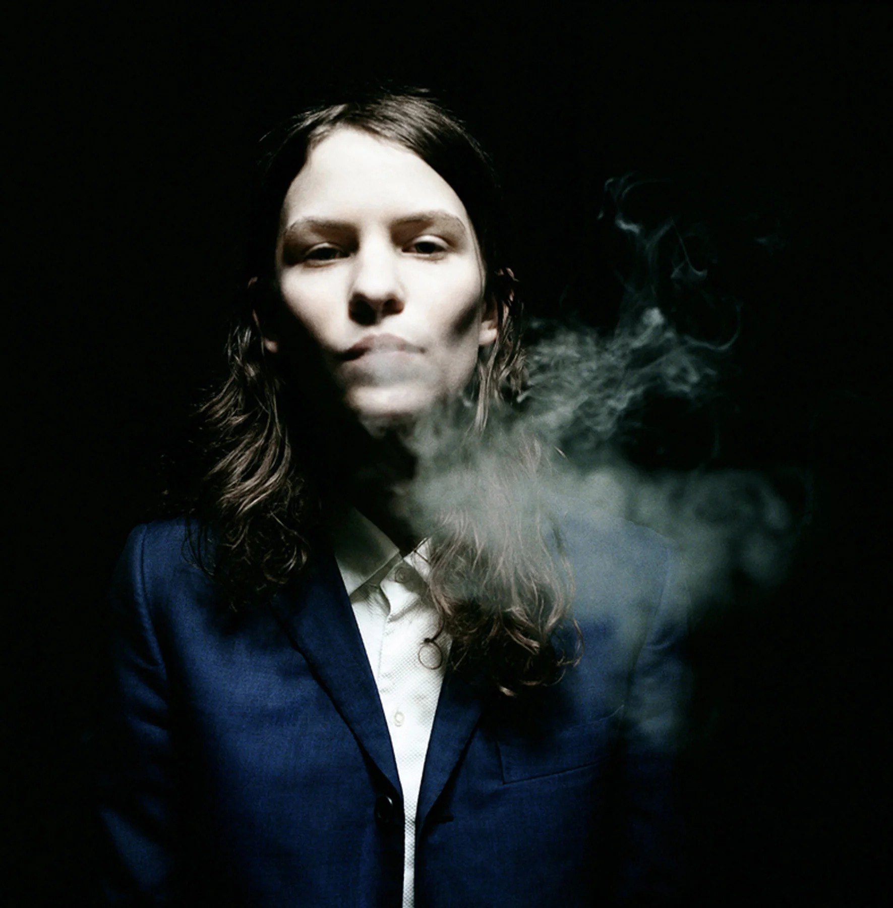 Portrait with dark hair and a cloud of smoke against black
