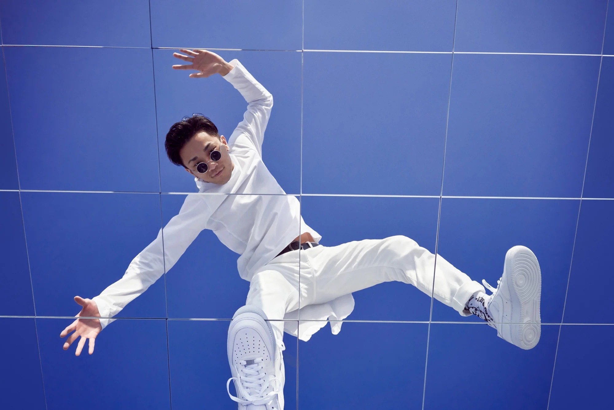 Figure in white suspended in a dynamic pose against a blue wall