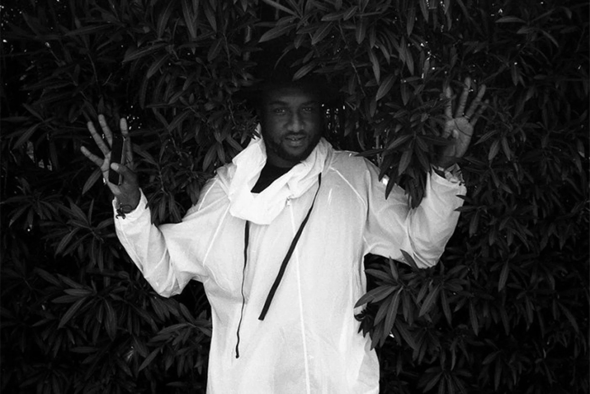 Black-and-white portrait of a figure in white with hands raised