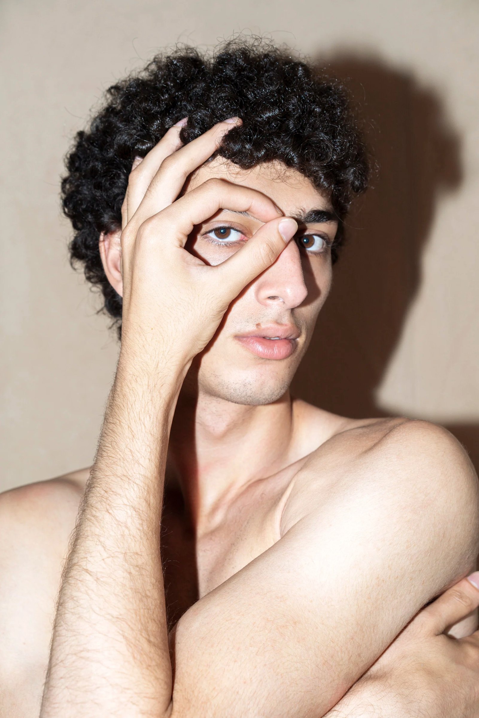 Qaher framing one eye with a hand against a pale wall