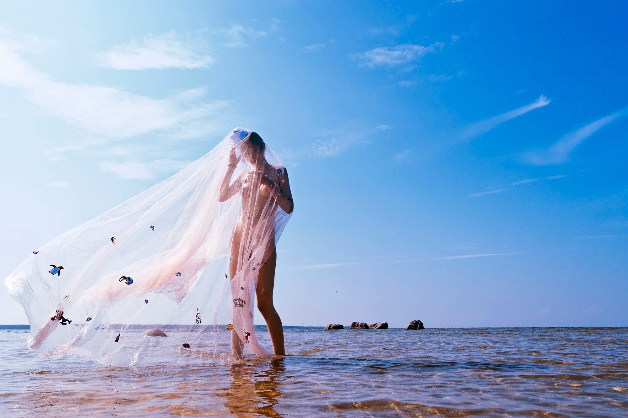 Veiled figure standing in shallow water beneath a blue sky