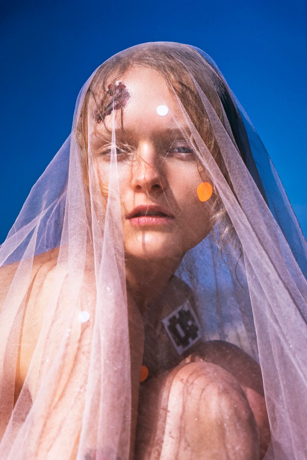 Close-up portrait beneath a translucent veil against blue sky