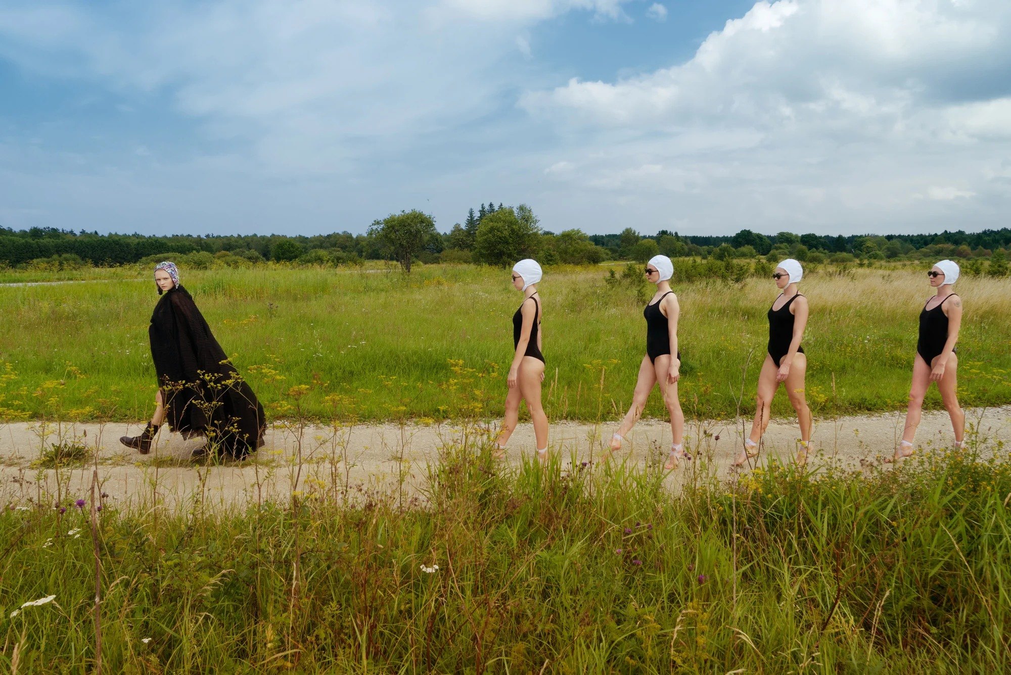 Line of figures crossing a green meadow
