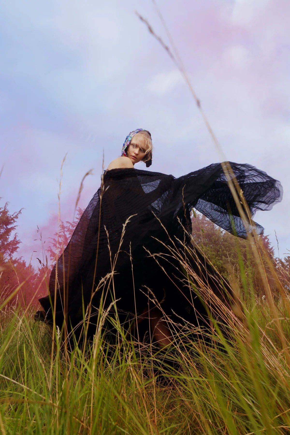 Figure in dark clothing amid tall grass and pale sky